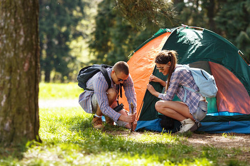 Two people setting up a tent surrounded by trees.