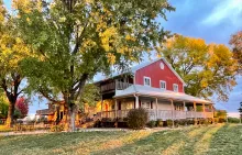 The Cellar Winery red building front wrap around porch with sun light filtering through full green trees