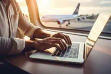 Close-up hand of a business man using a laptop while flying on an airplane near the window.