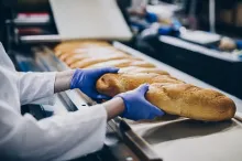 Gloved hands picking up a loaf of bread.
