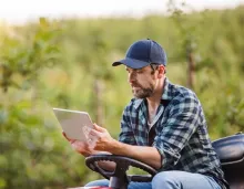 Man sitting on lawn mower holding iPad.