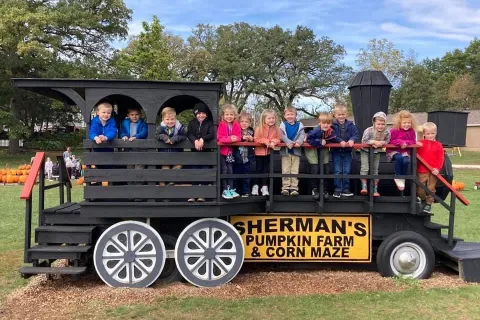 Kids smiling for photo op on train made of wood.