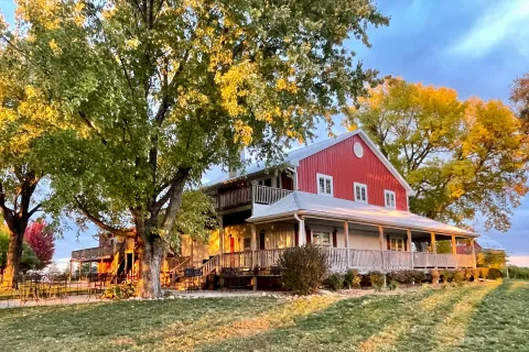 The Cellar Winery red building front wrap around porch with sun light filtering through full green trees